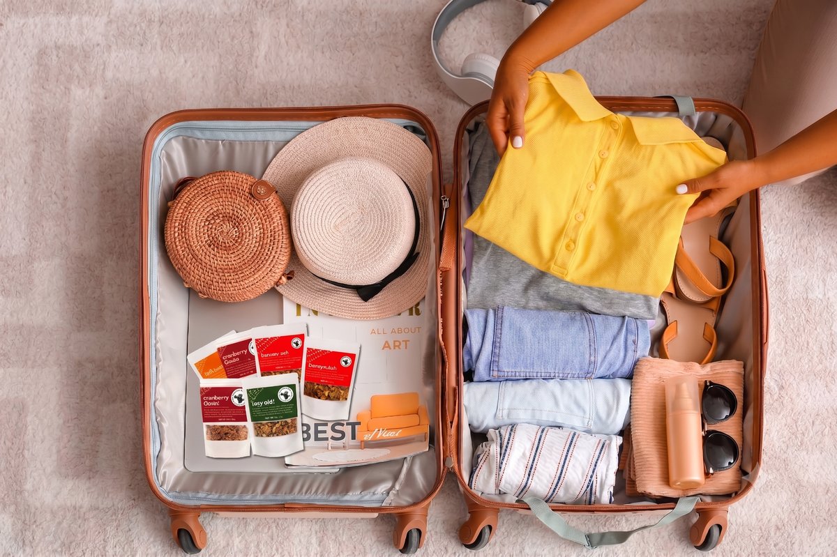 Open suitcase packed for a trip with clothes, sandals, and Flatbush Granola single-serving snack packs